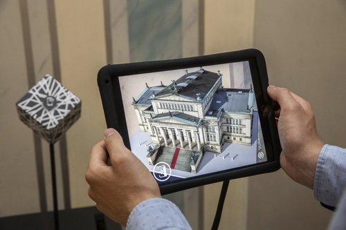 Ein Mann hält ein Tablet mit einem 3D Modell eines Gebäudes.